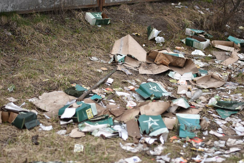 A large pile of mixed household rubbish and waste materials is collected on a paved urban street, placed in various black, red, and grey plastic rubbish bins and bags. Some bins are overflowing with i